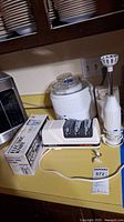 View of the kitchen appliances on a yellow countertop including the electric sharpener, hand blender, steamer insert, and boxed electric knife.