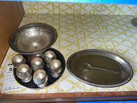 Overall view showing pedestal bowl on circle tray, six cordial cups on black tray, oval tray and spoon.