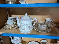 Teacups and saucers displayed on shelf with the 'Samaritaine' teapot center.