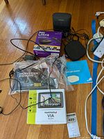 TomTom VIA 1605M GPS box showing product front with screen display and map details alongside Monster Power device in bag, Roku Ultra box, Bose speaker and other cables on hardwood floor.