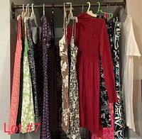 Full view of 15 assorted women's dresses hanging on a rack in various colors, patterns, and styles including floral, solid red knit, and sleeveless dresses.