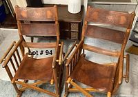 Two leather and wood rocking chairs side by side on a grey rug in front of a cabinet