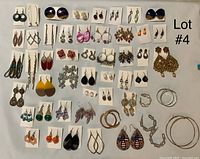 Wide view of many pairs of earrings arranged on a white surface showing a variety of styles including hoops, dangling earrings, studs, and colorful drops.