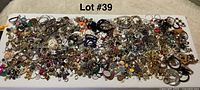 Wide view of a large assortment of broken and vintage costume jewelry spread out on a surface showing many small pieces like earrings, rings, and beads.