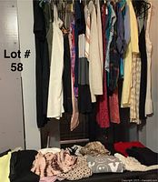 Photo of assorted women's clothing hanging on hangers and folded below, featuring a variety of colors and styles including knits and dresses.