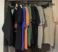 View of all 9 shirts hanging on a rack, showing various colors and designs including black, blue, orange, green, gray, and beige sweatshirt.