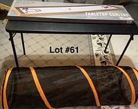 Photo of tabletop curling game in unopened box on table with black mesh pet tunnel below the table.
