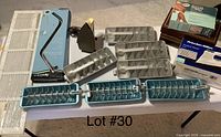 Photo of two vintage irons, seven vintage metal ice trays with dispensers, and some boxed items including a Lady Remington hair removal system and boxed knee brace.