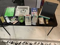 Wide view of entire lot on black table: includes iPad Pro Slim Folio case, green iPad cover, health and baby care products, vintage napkin holder, lotion tubes, and boxes.
