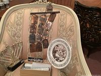 Overview of four Judaica items displayed on vintage upholstered chair, including copper wall hanging, decorative plate, and two boxed items.