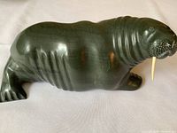 Side profile of dark green stone walrus sculpture showing body shape and surface finish