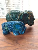 Two elephants side by side on wood surface with both visible in natural light.