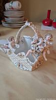 Cherubs basket angled showing three cherubs and handle, revealing detailed lattice design and gilded accents with some paint wear