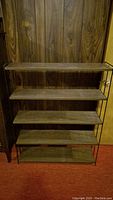 Front view of vintage metal frame bookcase with five wood shelves against wood panel wall and red carpet.