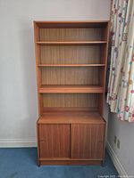 Front view of the vintage teak veneer bookcase showing three shelving levels and base cabinet with sliding doors.