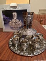 Wine divider set assembled on table with box in background, showing all pieces and ornate grapevine pattern.