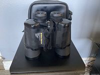 Front view of West Marine binoculars with visible brand label and carrying case behind.
