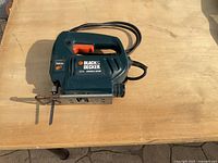 Front angled view of the used Black & Decker jigsaw on a wooden surface, showing the power cord and blade.