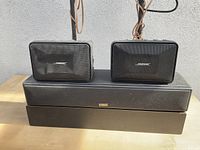Photo showing two small Bose satellite speakers placed on top of two longer Bose soundbar speakers with cables attached