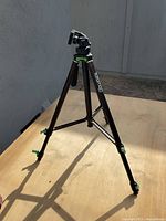 Photo of one camera tripod showing black extendable legs with green adjustment locks and a swivel camera mount head.