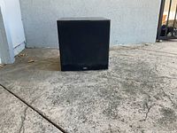 Front view of a single black cube speaker showing a mesh grille and NHT logo on the bottom center.