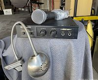 Front view of Pioneer MA-3 karaoke mixer with microphone and stand on cloth-covered surface in a garage or warehouse space.