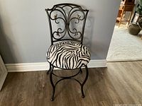 Front angle view of black metal dresser chair with zebra print seat and ornate backrest