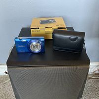 Photo showing the Fujifilm FinePix JZ250 blue camera, black protective case, and original box on a surface.