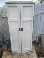 Front view of the closed white plastic garden storage shed with black handles and green base.