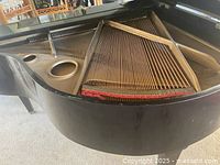 Grand piano open, showing strings and soundboard inside, black finish visible with some minor wear.