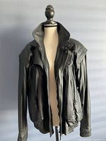 Front view of black leather bomber jacket on a mannequin against a gray wall