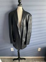 Front view of the men's black leather coat jacket on a mannequin, showing full length and style features like buttons and lapels.