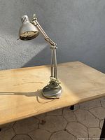 Silver flexible office desk lamp on wooden table, showing the side profile and coiled cord on weighted base.