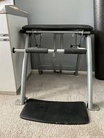 Front view of the Pilates chair showing black padded seat, foam padded side handles, silver metal frame, and foot platform.