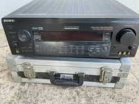 Front and top view of Sony digital audio/video control center placed on top of a silver hard case with handle.