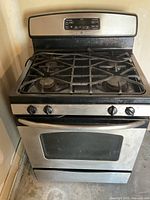 Front angled view of stainless steel GE gas stove with black trim, showing four burners and oven door with window.