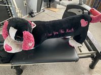 Side view of black and pink long sausage dog plush toy, showing embroidered text and heart design on body.