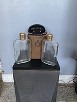 Photo of two ribbed glass bottles with gold caps alongside brown leather carrying case.