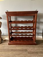 Photo of front view of wooden wine table rack showing four scalloped shelves for wine bottles and metal handles.