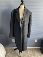 Front view of the grey wool coat displayed on a mannequin, showing the lapel collar, long sleeves, and button closure.