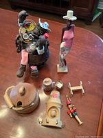 Photo showing a collection of assorted wooden decor items on a wooden table including figurines, teapot, and small accessories.