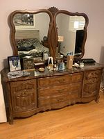Frontal view of large wooden bedroom dresser with two ornate mirrors, several drawers, and side cabinets with visible carved wood details.