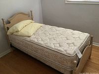 Single bed frame with boxspring and mattress showing floral quilted pattern and wooden headboard