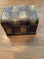 Full view of the decorative storage chest showing the patchwork pattern with aged and distressed patches and two leather straps.