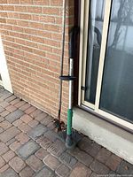 Electric garden trimmer and metal garden rake propped against exterior wall near sliding door.