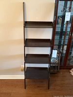 Full front view of black leaning wall shelf with four shelves.