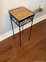 Full view of the square metal plant stand with decorative tile top, showing legs and metal scrollwork.