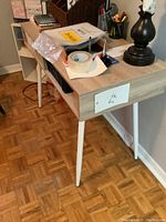 Side angle photo of the small desk showing light wood grain finish, white angled legs, and a narrow open shelf below the desk top.