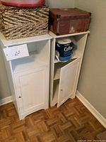Two white storage shelves with cupboard doors positioned side by side holding household items on top