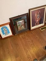 Three religious framed photos/artwork leaning against a wall on wooden floor.